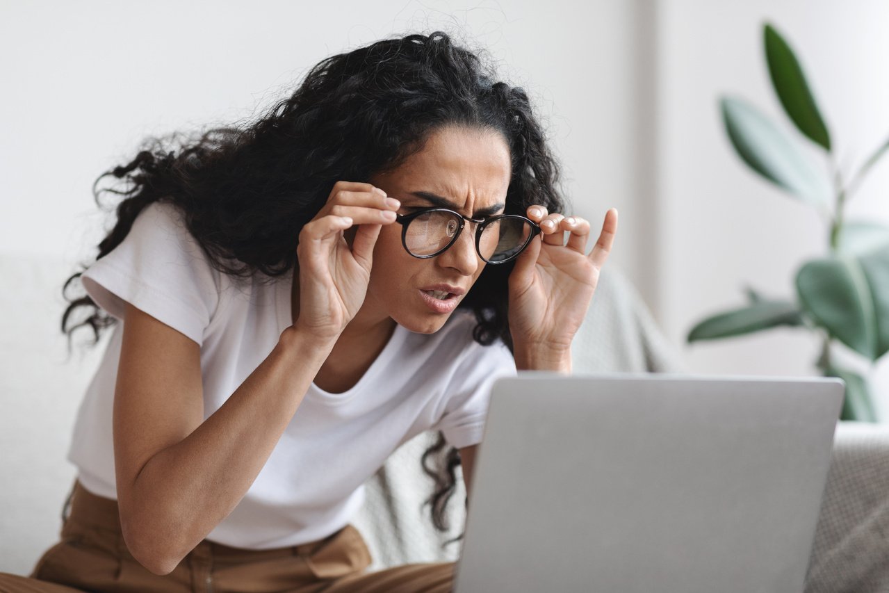 Young woman with bad eyesight using laptop, wearing glasses